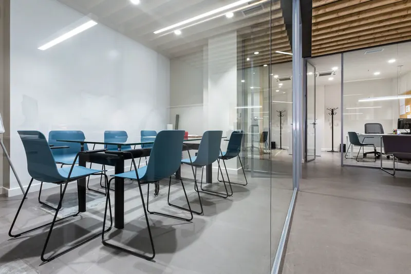 Sala de reuniones de Cuairón con mesa de vidrio y sillas azules, separada por una mampara acristalada