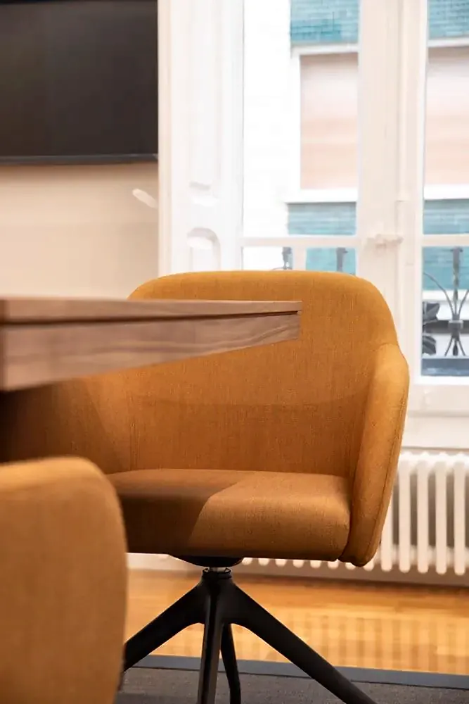 Detalle de una silla mostaza junto a la mesa, ante un balcón del edificio