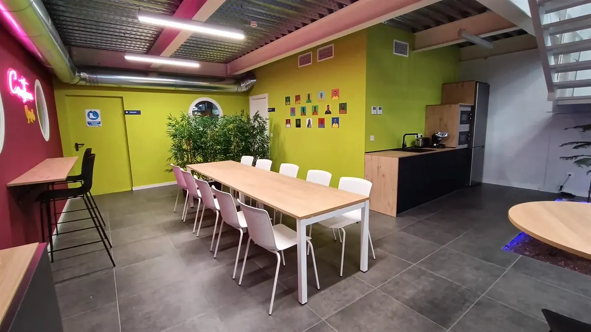Comedor con mesa larga, sillas blancas y pared amarilla, con el office al fondo