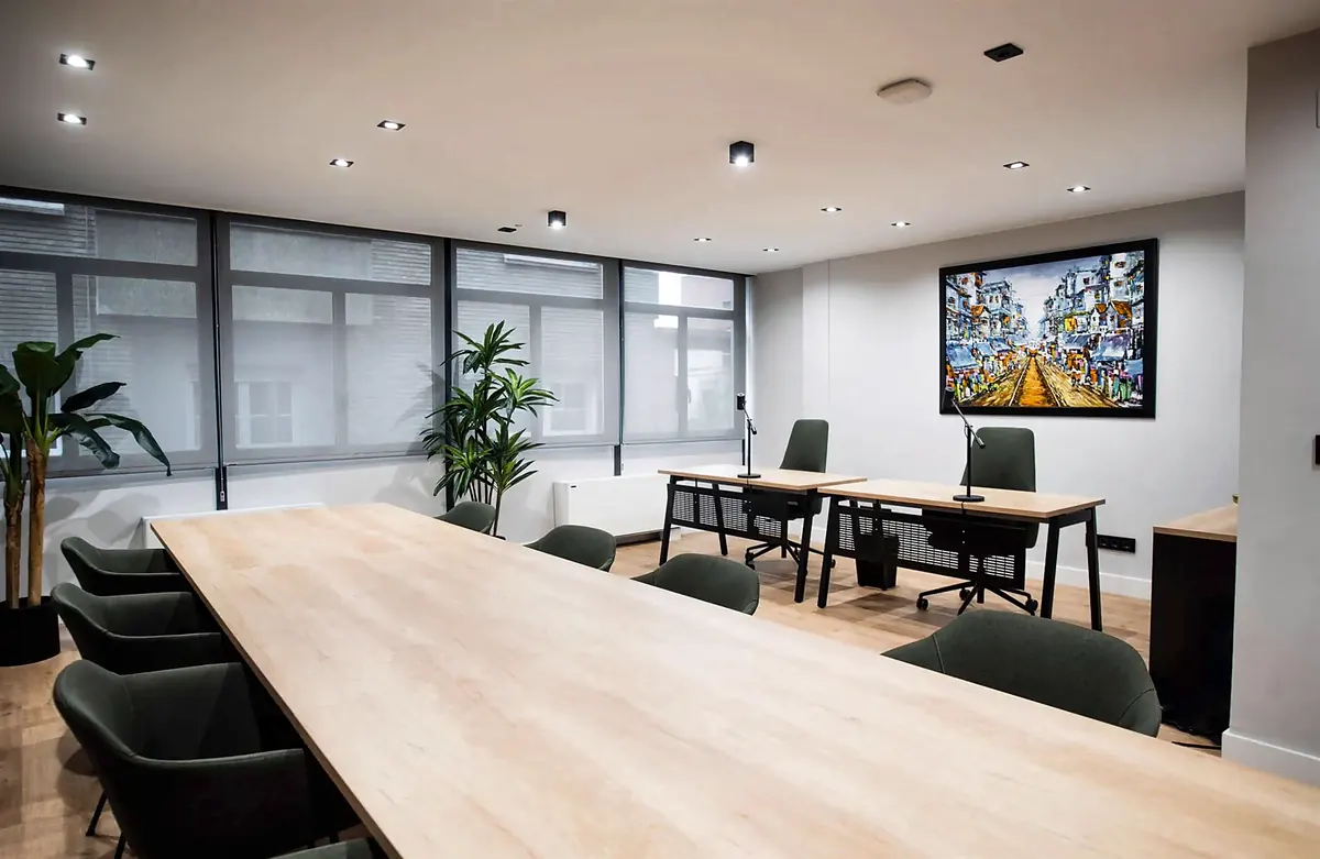 Oficina de LaudoFarma en Zaragoza: sala de reuniones con mesa larga de madera clara, sillas verdes y puestos junto al ventanal
