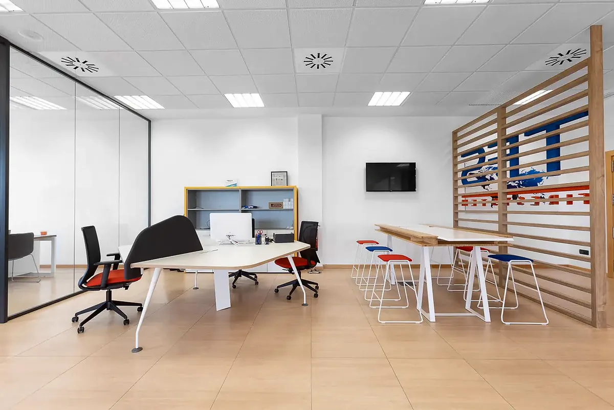 Zona de trabajo abierta con mesa alta, taburetes y celosía de madera con el logotipo